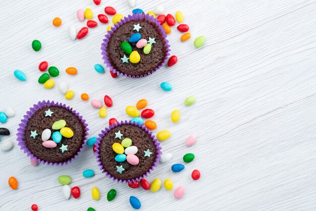 Una vista superior de deliciosos brownies dentro de formas púrpuras con caramelos de colores sobre blanco, dulces de color caramelo