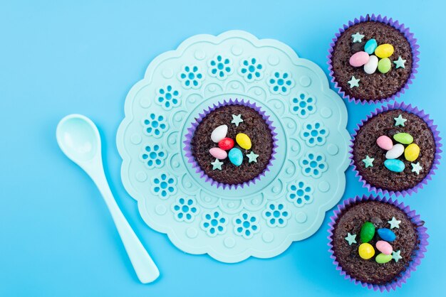 Una vista superior de deliciosos brownies dentro de formas púrpuras junto con caramelos de colores en dulces de color azul