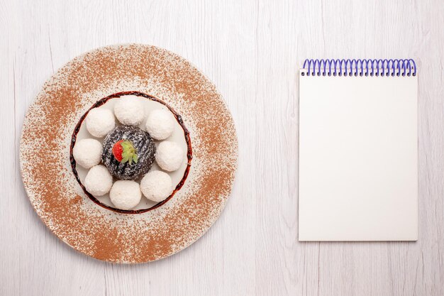 Vista superior de deliciosos caramelos de coco con pastel de chocolate en el escritorio blanco pastel galleta galletas dulces dulces