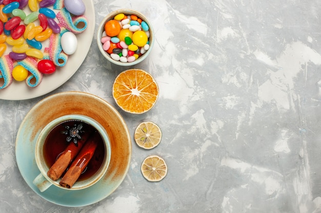 Vista superior de deliciosos caramelos de colores con mermelada y taza de té en la superficie blanca