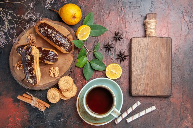 Vista superior deliciosos eclairs de choco con taza de té en pasteles dulces de postre de mesa oscura