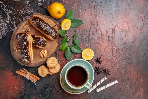 Vista superior deliciosos eclairs de choco con taza de té en pasteles dulces de postre de mesa oscura