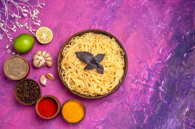 Vista superior de deliciosos espaguetis cocidos con condimentos en un plato de pasta de comida de masa de mesa de color rosa claro