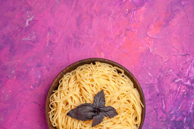 Vista superior de deliciosos espaguetis cocidos dentro de la placa en el plato de masa de pasta de comida de mesa rosa