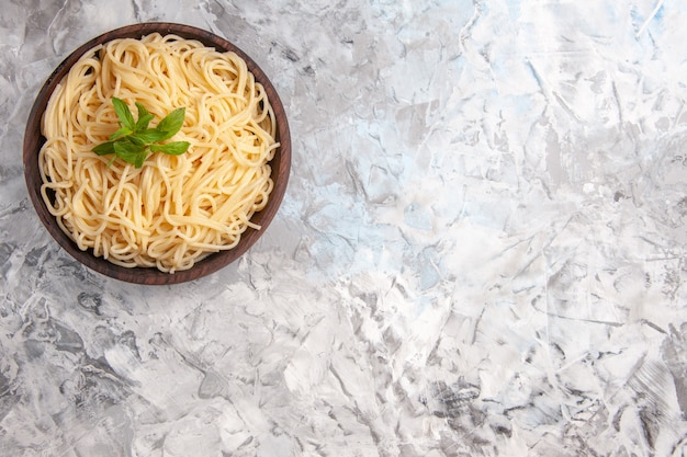Vista superior deliciosos espaguetis con hojas verdes en la masa de comida de pasta de plato de mesa blanca