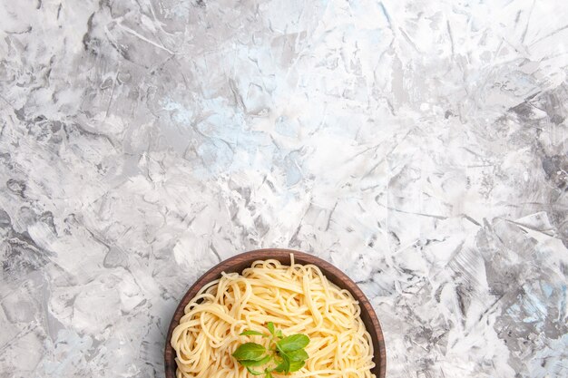 Vista superior deliciosos espaguetis con hojas verdes en la pasta de masa de comida de plato de mesa blanca