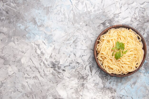 Vista superior de deliciosos espaguetis con hojas verdes en la pasta de masa de plato de comida de mesa blanca