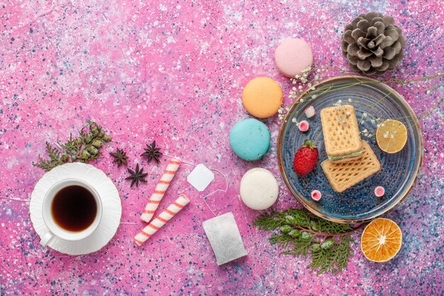 Vista superior de deliciosos gofres con deliciosos macarons franceses y té en el escritorio rosa