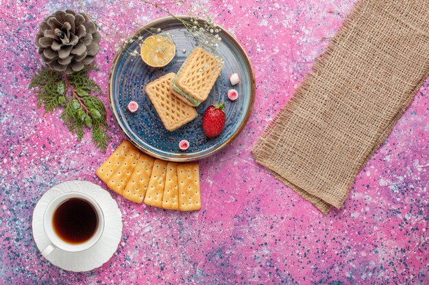 Vista superior de deliciosos gofres con galletas de macarons franceses y té en superficie rosa