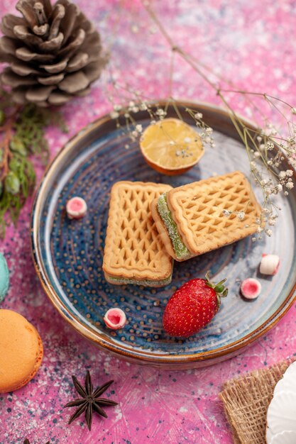 Vista superior de deliciosos gofres con macarons franceses en la superficie rosa