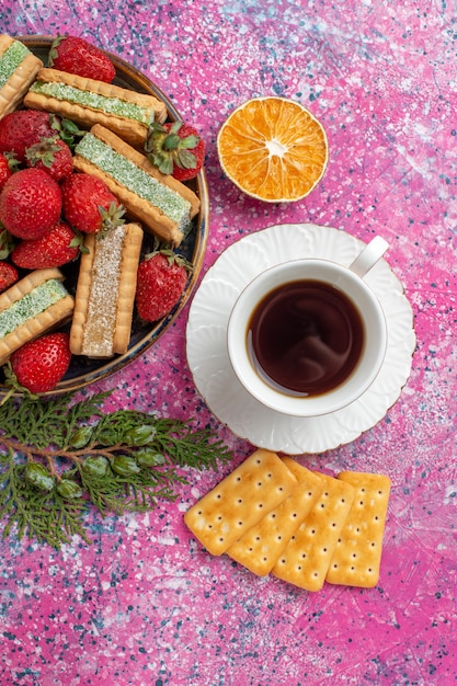 Vista superior de deliciosos gofres con taza de té y fresas rojas frescas en la superficie rosa