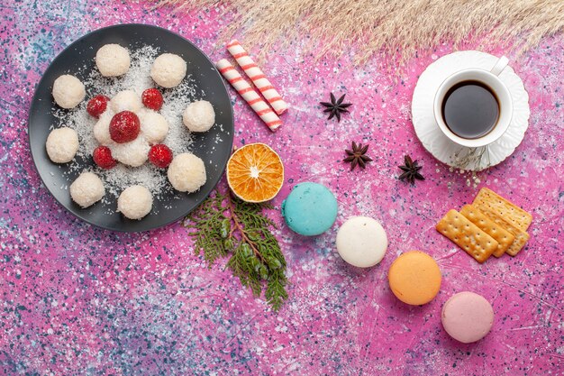 Vista superior de deliciosos macarons franceses con caramelos de coco y taza de té en superficie rosa