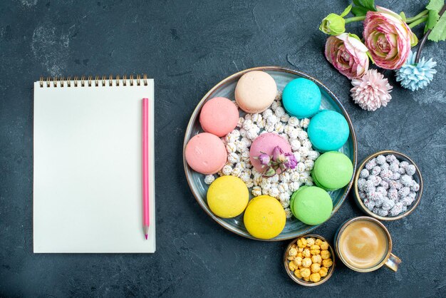 Vista superior deliciosos macarons franceses con caramelos dentro de la bandeja en el escritorio oscuro