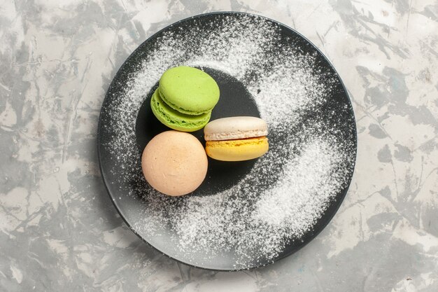 Vista superior deliciosos macarons franceses dentro de la placa sobre fondo blanco pastel galleta azúcar hornear pastel dulce