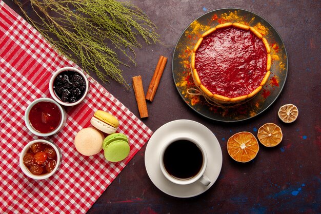 Vista superior deliciosos macarons franceses con mermeladas de frutas y una taza de café en el escritorio oscuro pastel de mermelada de frutas dulces galleta azúcar dulce