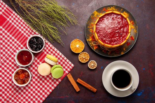 Vista superior deliciosos macarons franceses con mermeladas de frutas y una taza de café en la superficie oscura galleta de pastel de fruta dulce galleta de azúcar dulce