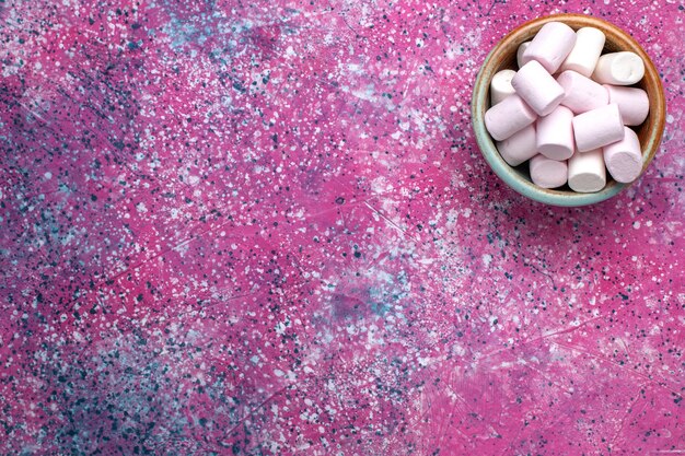 Vista superior de deliciosos malvaviscos dulces dentro de una olla redonda sobre superficie rosa