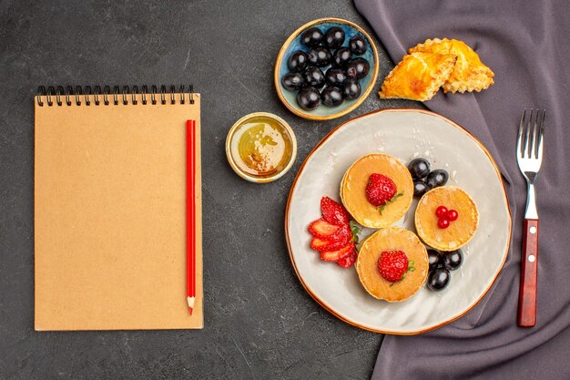 Vista superior deliciosos panqueques con aceitunas y frutas en la oscuridad