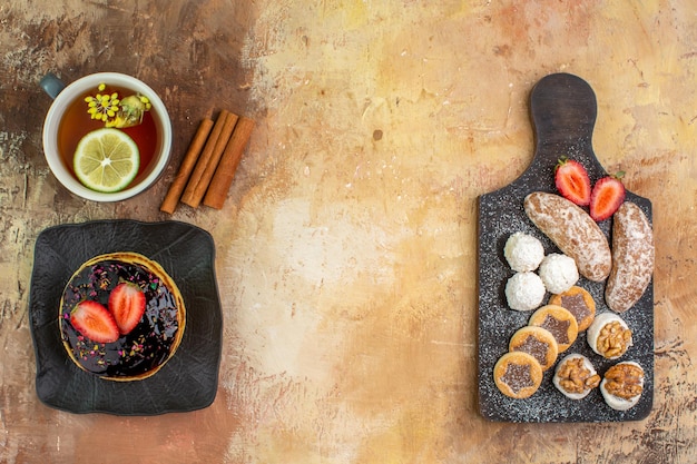 Vista superior deliciosos panqueques dulces con taza de té y dulces en la mesa de luz