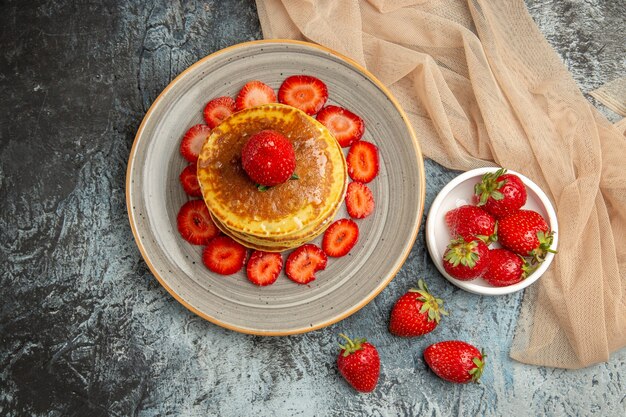 Vista superior deliciosos panqueques con fresas frescas en piso claro