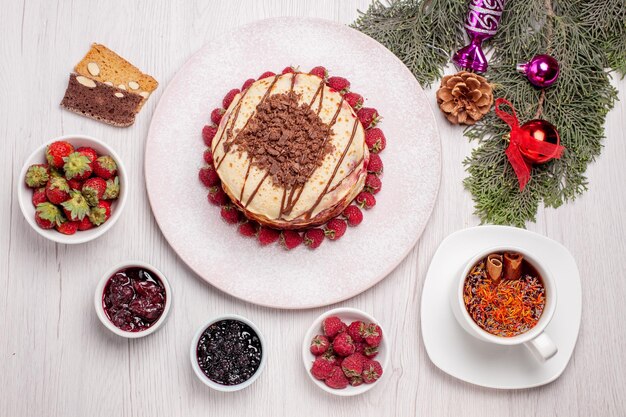 Vista superior deliciosos panqueques con fresas y una taza de té en el escritorio blanco pastel pastel galleta de frutas baya dulce