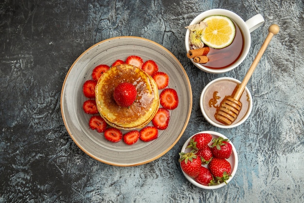 Vista superior deliciosos panqueques con fresas y taza de té a la luz