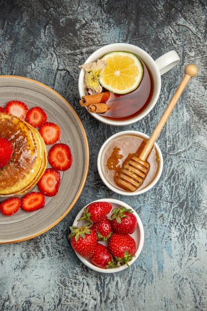 Vista superior deliciosos panqueques con fresas y una taza de té en la mesa de luz pastel de frutas dulce
