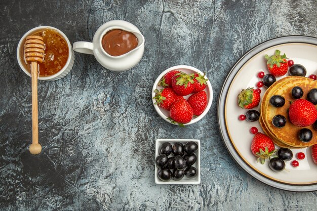 Vista superior deliciosos panqueques con frutas frescas y miel a la luz