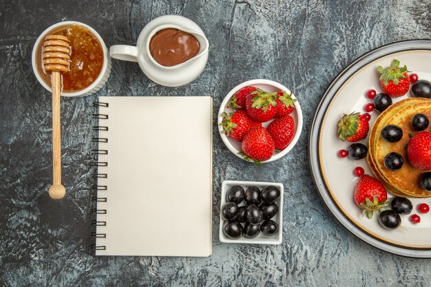 Vista superior deliciosos panqueques con frutas frescas y miel a la luz