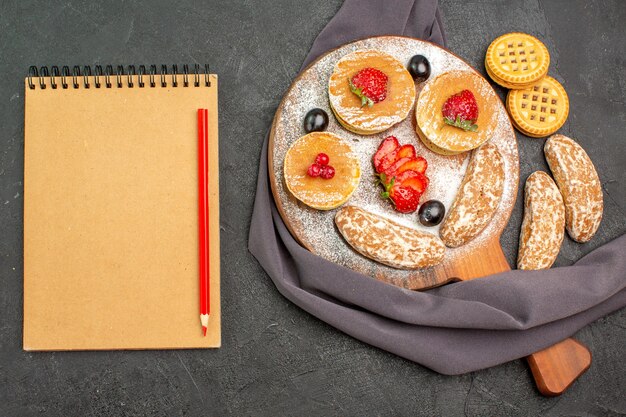 Vista superior deliciosos panqueques con frutas y pasteles dulces en el postre de pastel de superficie oscura dulce