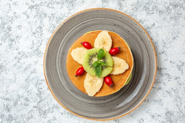 Vista superior deliciosos panqueques con frutas en rodajas dentro de la placa en la superficie blanca fruta postre dulce pastel de azúcar color de desayuno