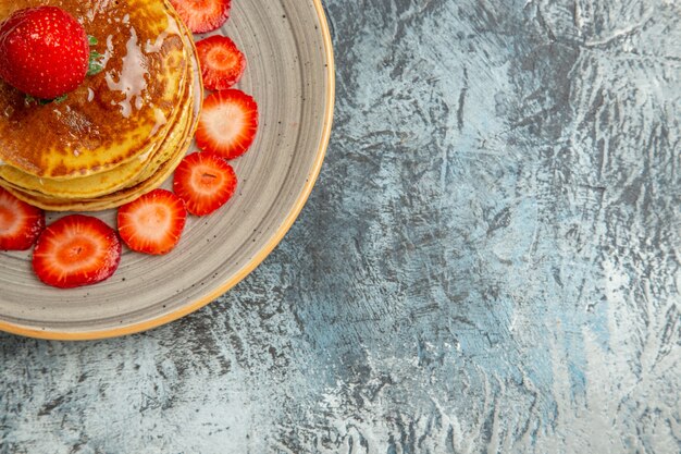 Vista superior deliciosos panqueques con miel y fresas a la luz