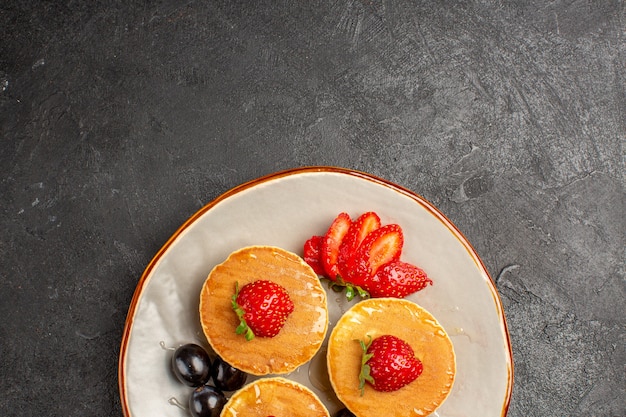 Vista superior deliciosos panqueques poco formados con frutas en pastel de pastel de frutas de piso oscuro