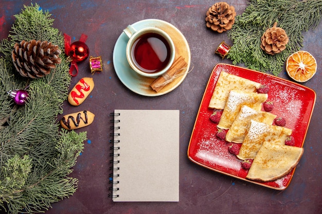 Vista superior de deliciosos panqueques con taza de té y frambuesas en negro