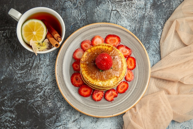 Vista superior deliciosos panqueques con taza de té y frutas a la luz