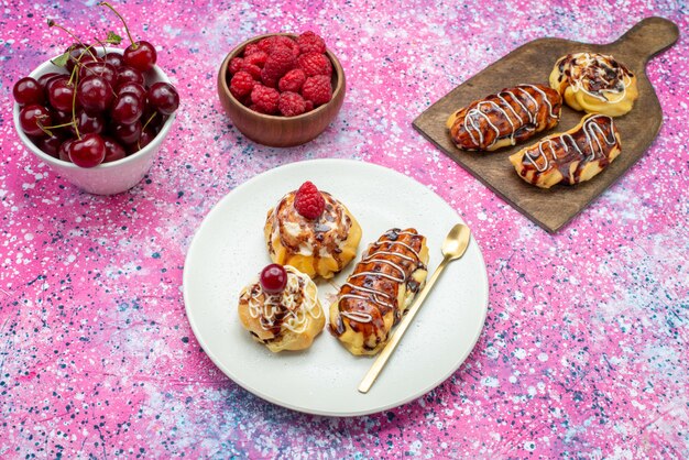 Vista superior deliciosos pasteles afrutados con crema y chocolate dentro de la placa blanca junto con frutas frescas en el fondo rosa pastel galleta dulce hornear