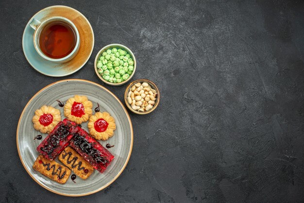 Vista superior deliciosos pasteles afrutados con galletas y una taza de té en el fondo oscuro pastel de galletas de azúcar galleta pastel de té dulce