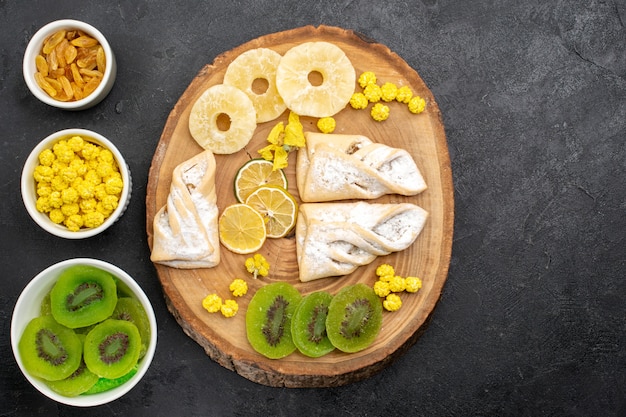 Vista superior de deliciosos pasteles con anillos de piña secos y kiwis en el escritorio gris