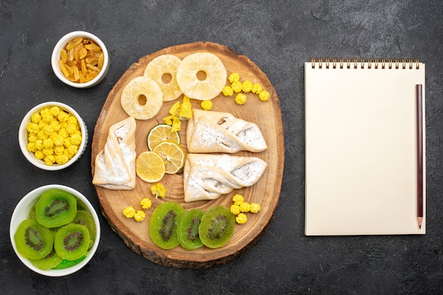 Vista superior de deliciosos pasteles con anillos de piña secos y kiwis en el escritorio gris