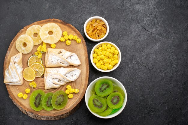 Vista superior de deliciosos pasteles con anillos de piña secos y kiwis en el escritorio gris