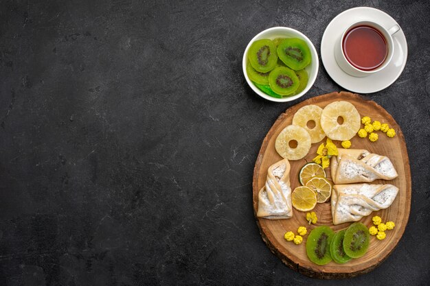 Vista superior de deliciosos pasteles con anillos de piña secos y kiwis en un espacio gris oscuro