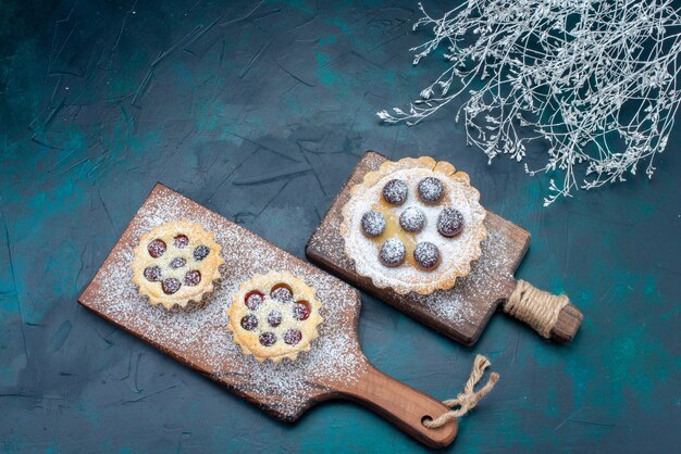 Vista superior de deliciosos pasteles de azúcar en polvo con frutas en el escritorio azul oscuro, pastel de galleta azúcar dulce