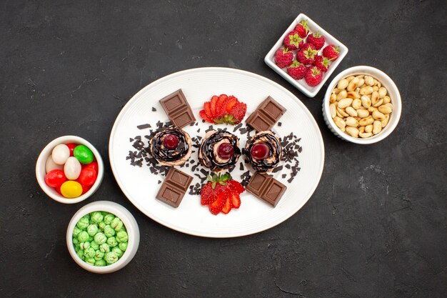 Vista superior deliciosos pasteles con barras de chocolate, caramelos y nueces en la superficie oscura pastel de frutas pastel de nueces baya de galleta
