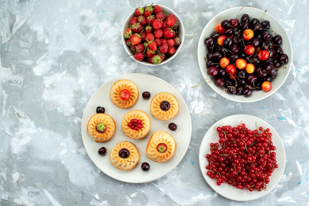 Una vista superior de deliciosos pasteles con bayas y frutas dentro de las placas pastel de azúcar de galleta