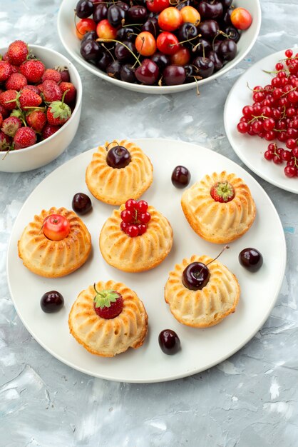 Una vista superior deliciosos pasteles con bayas y frutas dentro de las placas pastel de azúcar de galleta