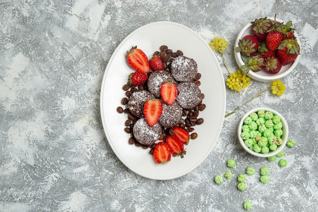 Vista superior de deliciosos pasteles de chocolate con caramelos y fresas en la superficie blanca galleta pastel de azúcar galleta de té dulce