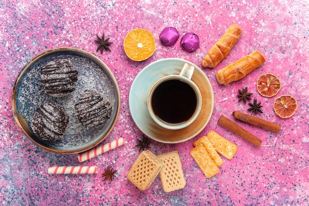 Vista superior deliciosos pasteles de chocolate con dulces y taza de té en rosa
