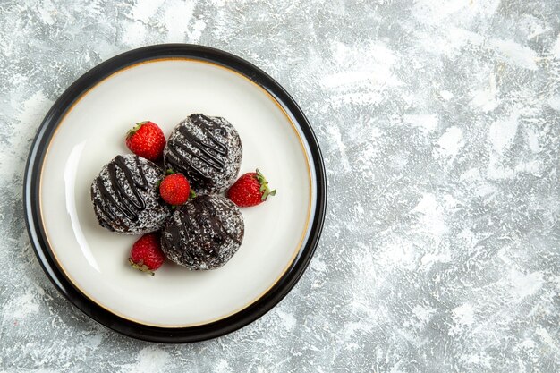 Vista superior deliciosos pasteles de chocolate con fresas rojas frescas sobre superficie blanca