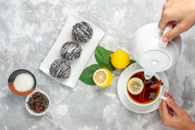 Vista superior de deliciosos pasteles de chocolate, pequeños y redondos formados con limón y una taza de té en la superficie blanca clara, galletas de pastel de frutas, galletas de azúcar dulce para hornear