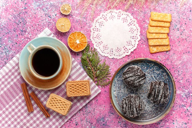 Vista superior de deliciosos pasteles de chocolate con taza de té y gofres en rosa claro